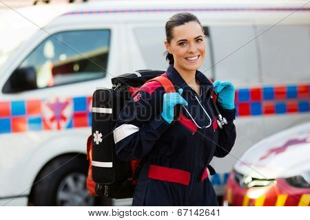 beautiful young female paramedic carrying lifepack in front of ambulance
