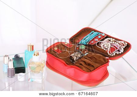 Handbag with accessorises and perfumes in bottles on table on  home interior background