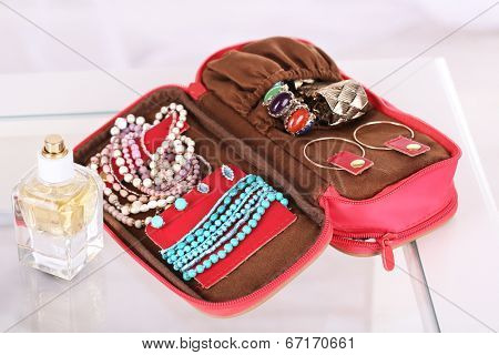 Handbag with accessorises and perfumes in bottles on table on  home interior background