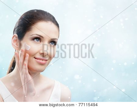 Woman applying cream on her face, winter background. The pursuit of beauty