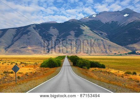  Smooth asphalt road passes between the yellow plains to the distant mountains. Steppes of Patagonia