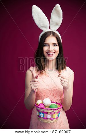 Smiling beautiful woman with an Easter egg basket over pink background. Looking at camera 