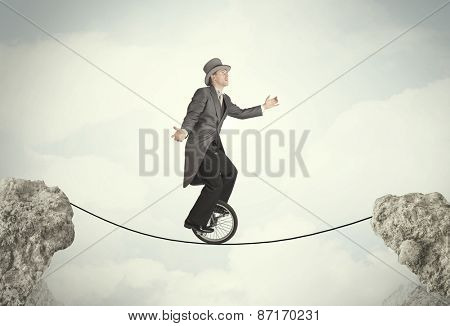 Brave business man riding an mono cycle between cliffs concept