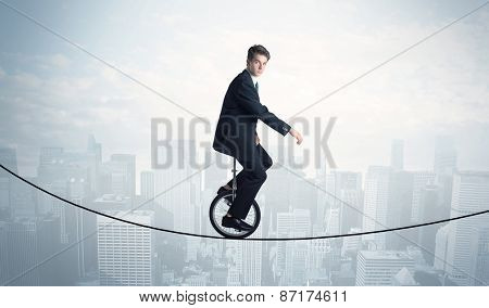 Brave guy riding a monocycle on a rope above cityscape concept