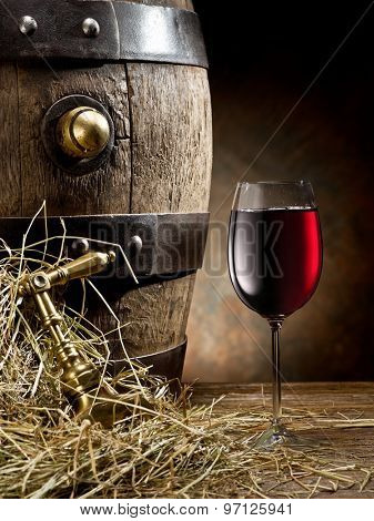 Still-life with glass of wine and barrel on the table in the cellar.