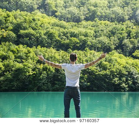 Young man, arms spread open enjoying freedom in front of lake