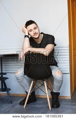 Young man in trendy spring outfit reaxing at modern cafe with white walls. Looking straight.