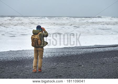 People walks and photographing on Reynishverfisvegur, Reynisfjara black sand beach with rocks, ocean and dark rain and storm clouds near the village of Vik in Iceland.