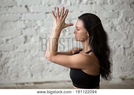 Portrait of middle aged yogi attractive woman practicing yoga concept, making namaste gesture with her eyes closed, working out, wearing black sportswear bra, close up, white loft background