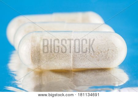 White capsules of glucosamine chondroitin healthy supplement pills on blue glossy background macro image
