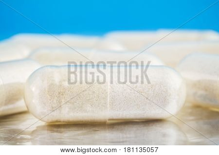White capsules of glucosamine chondroitin healthy supplement pills on blue glossy background macro image