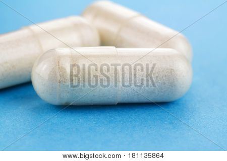 White capsules of glucosamine chondroitin healthy supplement pills on blue background macro image