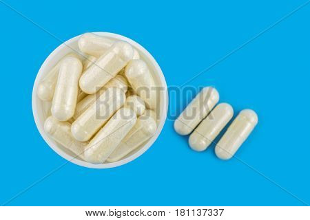 White capsules of glucosamine chondroitin healthy supplements pills in round bottle on blue background top view