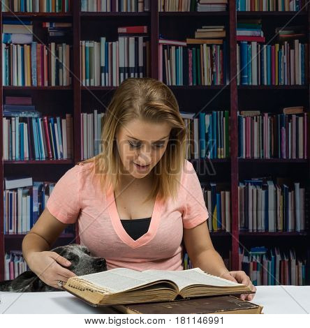 Young woman reads a book in a library while a dog sits next to her