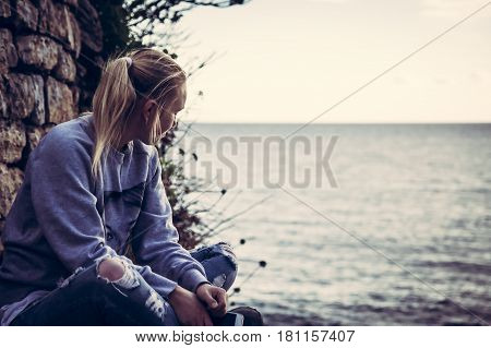 Thoughtful lonely young woman tourist with closed eyes thinking during her travel sitting on seashore in retro vintage style