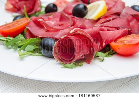 a white dish of bresaola and aragula