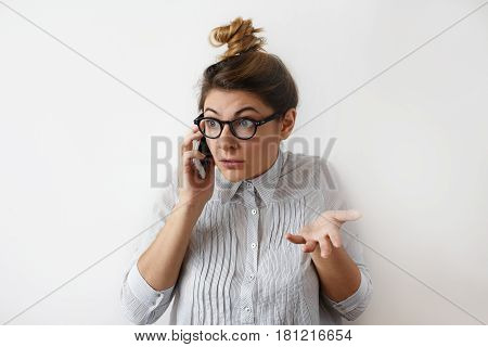 Portrait of a young woman european appearance with hair bun wearing white striped shirt ang glasses arguing on the phone with her boss. Negative human facial expression, business and problems concept