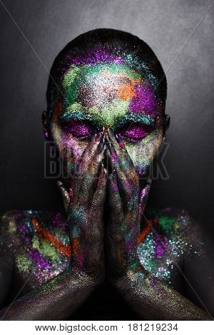 Young artistic woman in black paint and colourful powder. Glowing dark makeup. Creative body art on the theme of space and stars. Bodypainting project: art, beauty, fashion