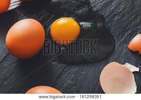 Fresh chicken brown home eggs with cracked eggshell and yolk on rustic slate black background. Closeup. Natural healthy food and organic cooking ingredients