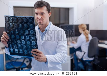 Diagnostic study. Serious professional male doctor standing in the staffroom and examining the X ray images while working in the oncology department