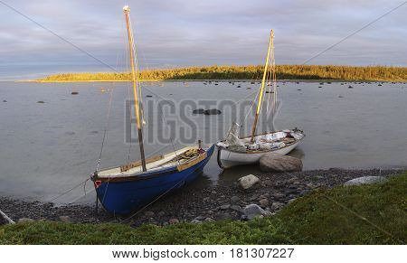 Fishing boats off the coast of the White Sea during the tide. Two old beached wooden rowing boats white and blue weathered and beaten on the shore