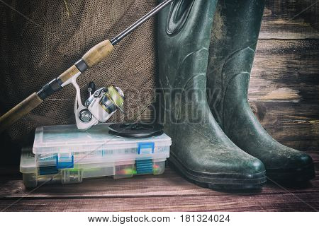 Fishing concept. Fishing tackles in boxes, rod, reel, fishing cage with rubber boots on timber board background. Toned image.