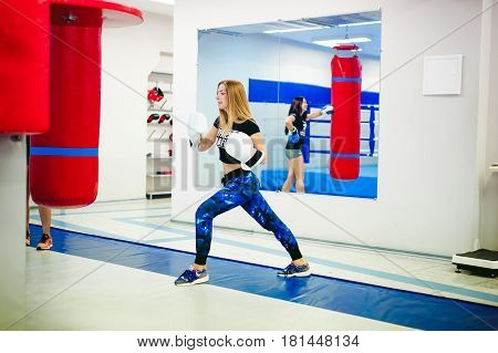 Young Woman Exercising In The Gym On Punching Bag. Two Girls Are Engaged In Martial Arts Training, P