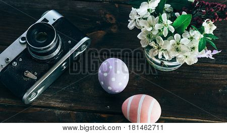 Preparation for Easter. Colorful handmade Easter eggs, paint, retro camera and vase with flowers on a wooden background