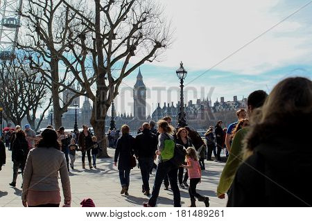 Big Ben visible in the background as crowds walk along South Bank in London on a sunny but cold spring day - blue skies and clouds