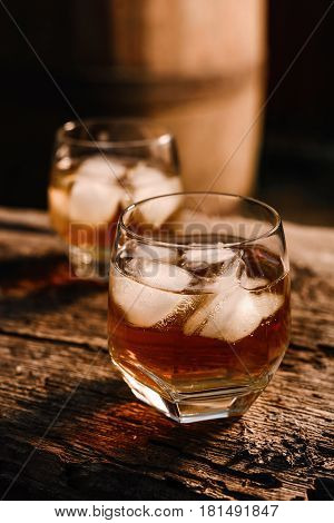 A glass of whiskey with ice on a wooden background close-up in the background of a barrel of whiskey