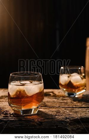 A glass of whiskey with ice on a wooden background close-up in the background of a barrel of whiskey