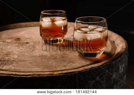 A glass of whiskey with ice on a wooden background close-up in the background of a barrel of whiskey