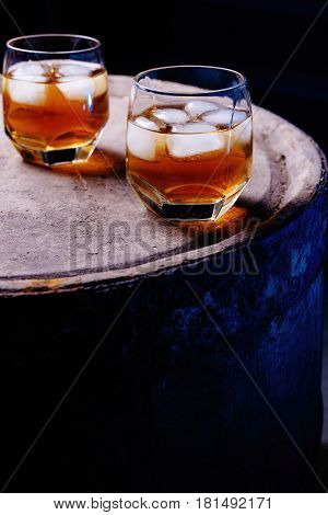 A glass of whiskey with ice on a wooden background close-up in the background of a barrel of whiskey