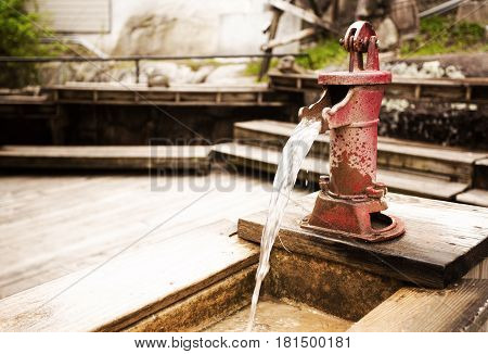 A small red vintage steel water pump mounted on a plank of wood with water pouring out of the spout