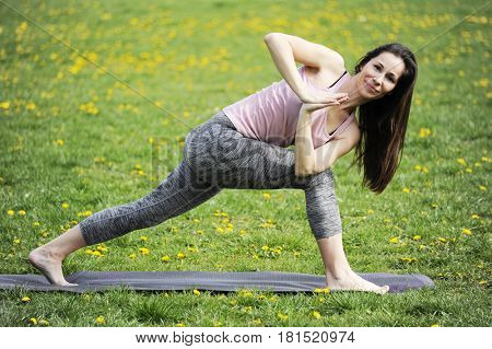 Young woman doing yoga in morning park. Parivritta parsvakonasana with namaste. Healthy lifestyle outdoor conception. 