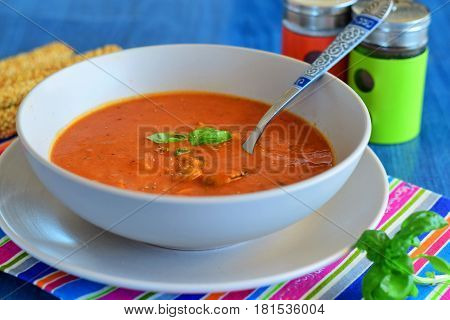 Tomato soup with mussels in a blue bowl on a blue background with bread sticks. Healthy eating concept