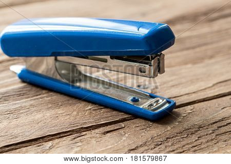 blue stapler on wooden background, close-up isolated