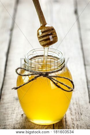 Honey jar with dipper and flowing honey on a wooden background and