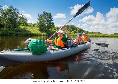 Two women with oars and little boy sail on inflatable boats on river at sunny summer day