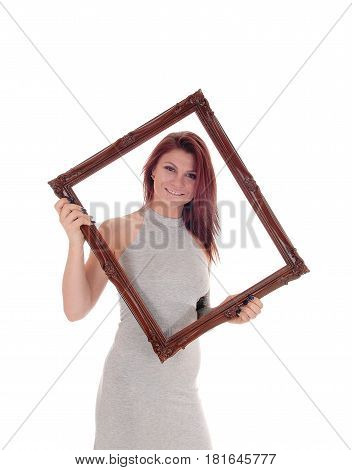 A beautiful young woman standing in a gray dress holding a picture frame looking through isolated for white background.