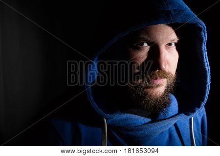 Solid bearded middle-aged man in a hood  portrait on black background