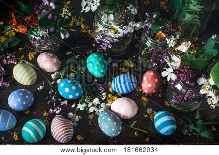 Picturesque bouquets of colorful spring  flowers in glass vases bottles and colorful handmade paint easter eggs on a dark wooden