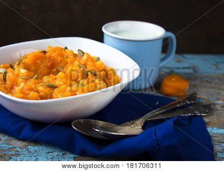 Pumpkin porridge in a white plate with a mug of milk on a blue wooden background