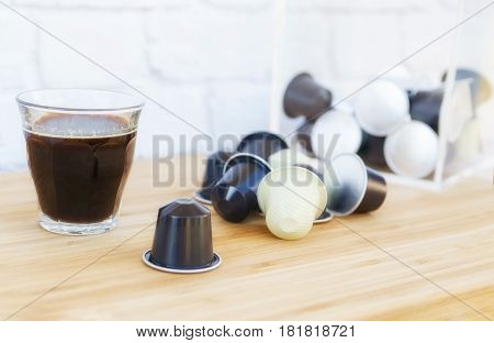 Cup of black coffee with foam and coffee capsules on wooden background.