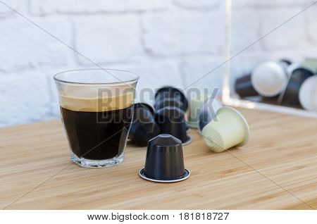 Cup of black coffee with foam and coffee capsules on wooden background.