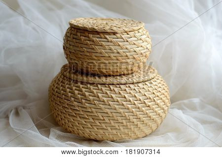 Wicker round baskets on a background of delicate tissue. Rural weaving with natural straw. Weaving from natural plants. Ecological items for the home.