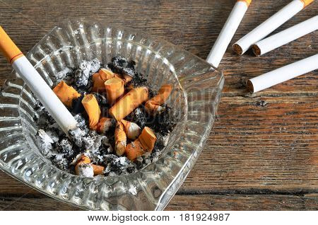 A close up image of a glass ashtray with lit cigarettes and cigarette ashes.