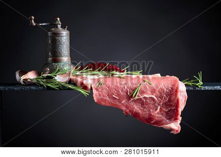 Raw Beef Steak With Peppermill, Garlic And Rosemary. Black Background, Copy Space.