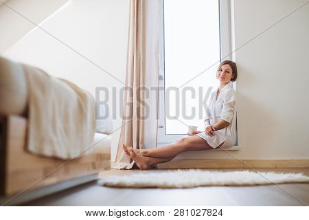 A Young Woman With Night Shirt Sitting By The Window In The Morning.