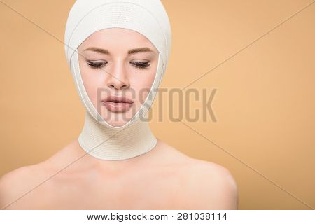 Naked Young Woman With Bandages Over Head Looking Down Isolated On Beige